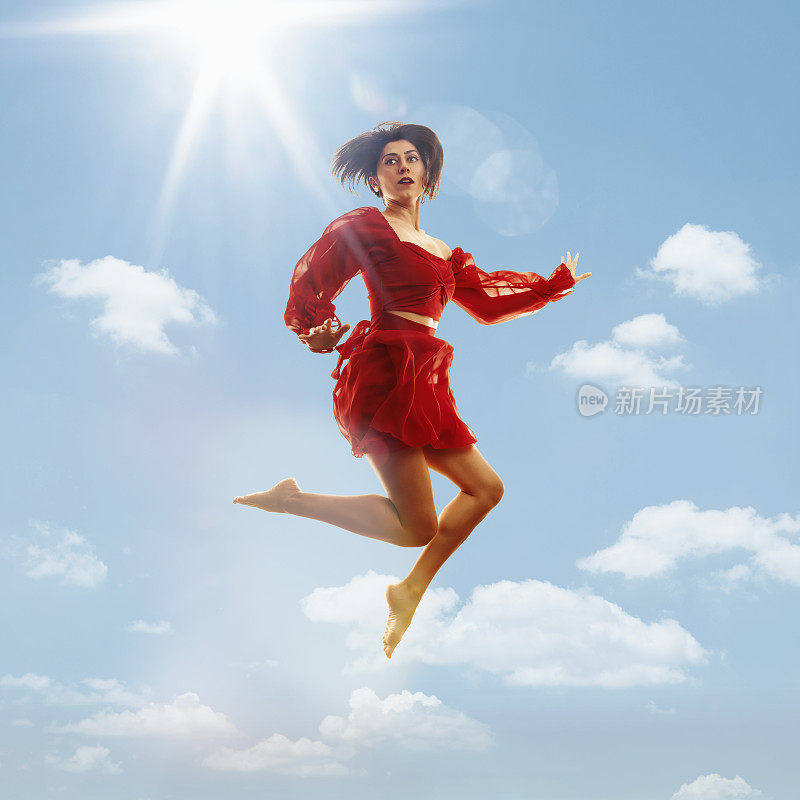 身着红色连衣裙的年轻女子在空中跳跃，蓝天和太阳为背景