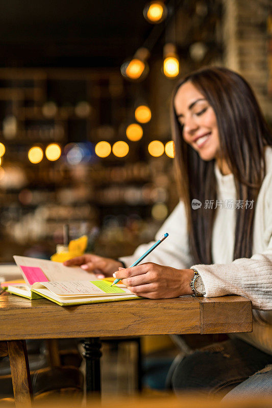 快乐的年轻女子在咖啡馆学习。