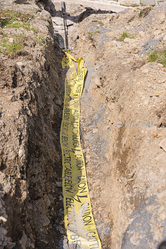 黄色警示胶带覆盖在为建筑物供电的壕沟中的电缆上。