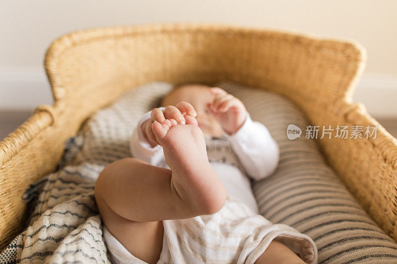 一个19周大的男婴躺在一个舒适的纱布毛毯里，躺在一个海草摩西篮子里
