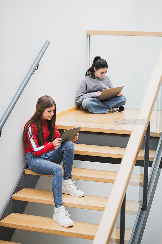 高中楼梯上的女孩们拿着笔记本和平板电脑。