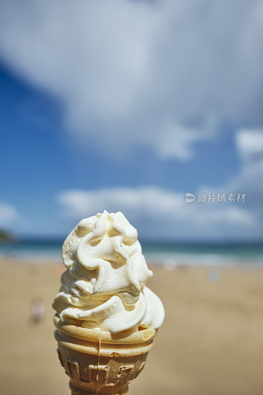 6月一个阳光明媚的日子，在康沃尔郡纽基的托万海滩，一只手拿着冰淇淋蛋筒。