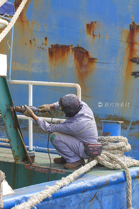 船坞区，一名工人正在用电锯打磨生锈的油船尾梯
