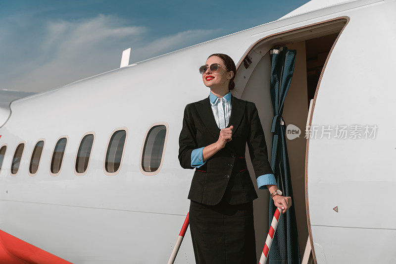 戴着墨镜的女空姐站在机场的飞机楼梯上，看着别处