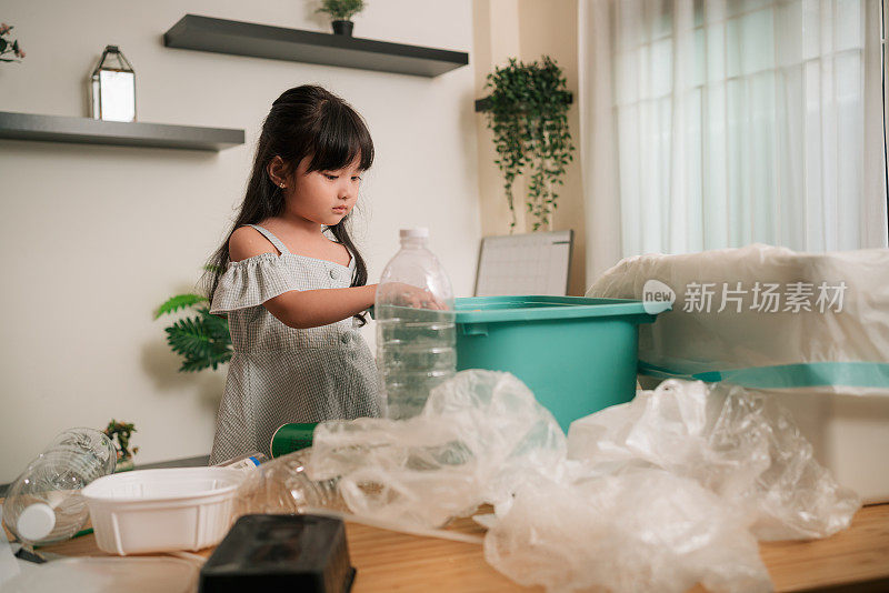蹒跚学步的小女孩正在整理垃圾以便回收。环保回收工作