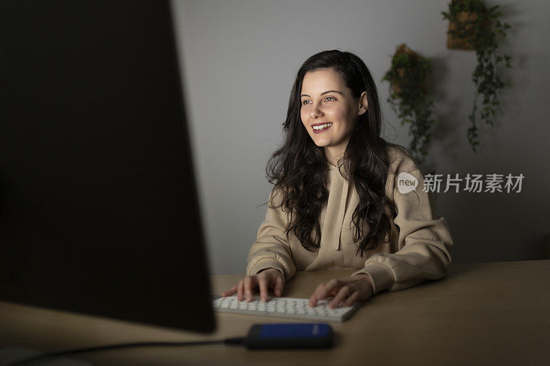 女性坐在家庭办公室的办公桌前，用笔记本电脑工作到深夜;在家远程加班的女性网页设计师