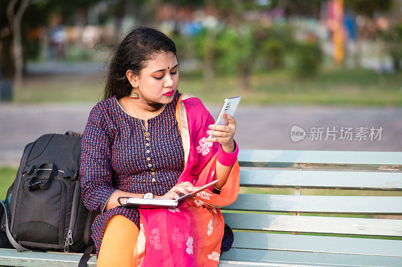 有吸引力的年轻白人女子坐在木凳上，在公园写日记。