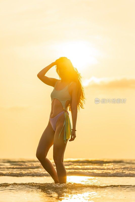 日落时分，沙滩上阳光灿烂。美丽的白人女子在海滩上的比基尼与精湛的日落和阳光在后面