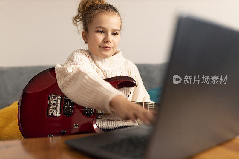 专注的年轻女孩在家里玩电吉他与笔记本电脑