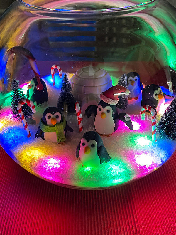 自制雪花球的特写图像，南极景象翻糖糖衣人物在玻璃圆顶被彩色串灯照亮，白色的冰屋，企鹅与红色的泡泡帽，绿色围巾和红色耳罩，人造树，重点在前景