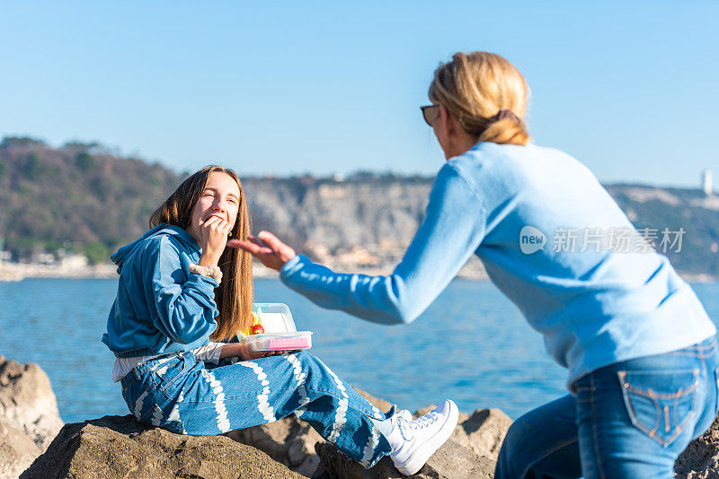 阳光明媚的冬日，母亲和十几岁的女儿在岩石海滩上野餐的快乐时刻