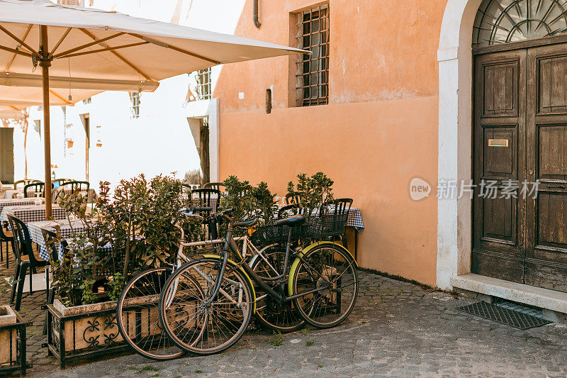 自行车停在街上。家里的旧自行车靠在橘黄色的墙上。城市交通概念。茂盛的绿色植物生长在房子门口的花盆里。意大利罗马特拉斯提弗列舒适的老街。