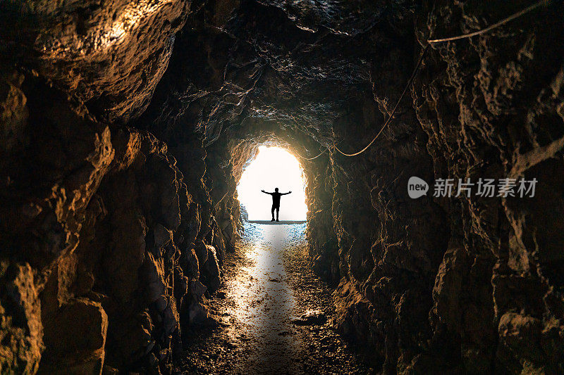 人影站在天然洞穴的尽头，地下隧道和灯光闪耀