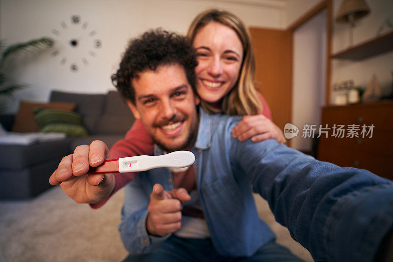 年轻的白人夫妇微笑着对着相机高兴地抱着怀孕的宝宝。