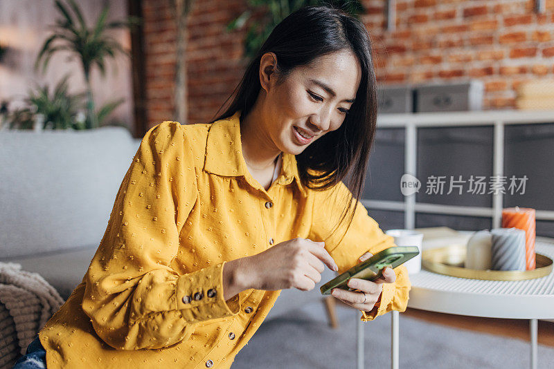 年轻的日本女子坐在地板上玩智能手机