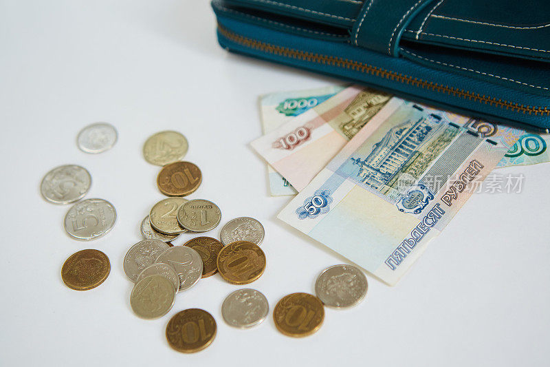 蓝色钱包旁边放着50卢布、100卢布和1000卢布的俄罗斯纸币，附近还散落着各种面值的硬币。节约和节俭的观念