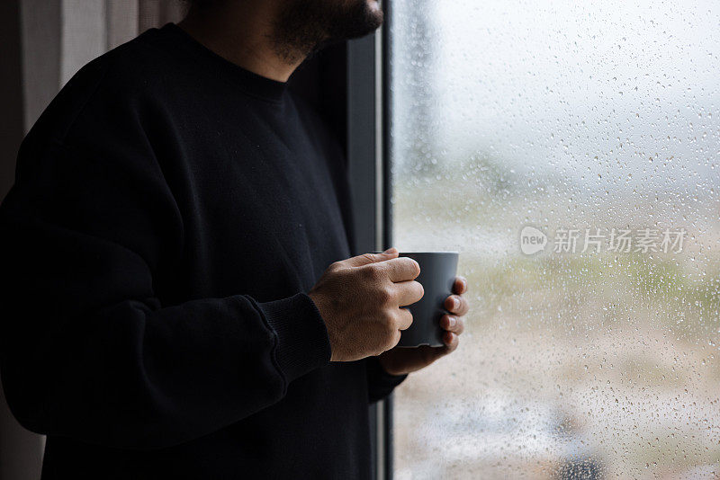 男子端着咖啡杯，望着远方的家