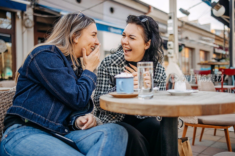 两个年轻女子坐在咖啡馆外面喝咖啡