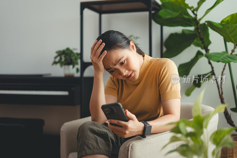 亚洲女性坐在家里看智能手机屏幕，有问题。