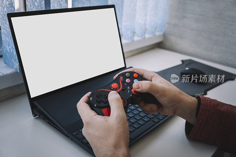 打开笔记本电脑，在家里的桌子上有一个空白的屏幕和一个视频游戏控制器。男人手里玩的操纵杆