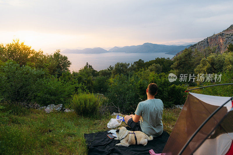 男人和狗的后视图考虑神奇的日落露营与海景