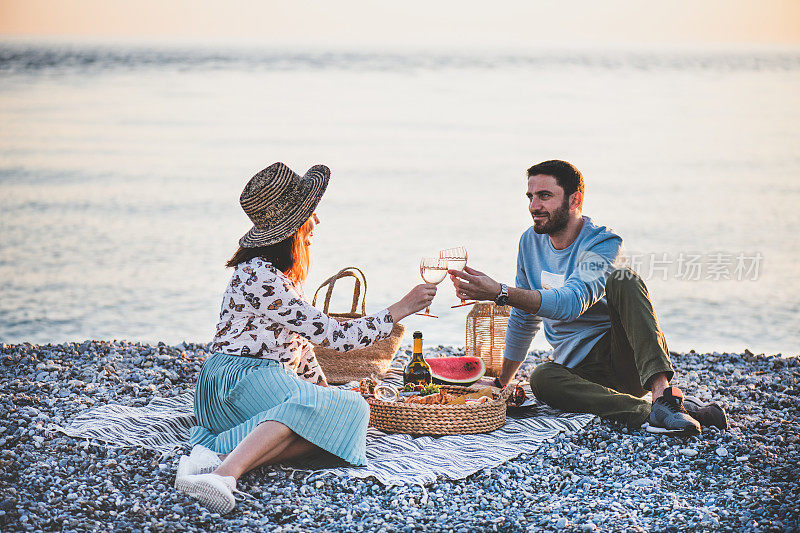 年轻幸福的夫妇在海边野餐和起泡酒