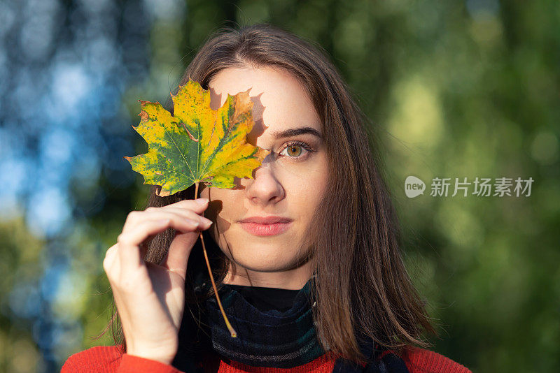 一个年轻女子举着一片落叶挡在眼前