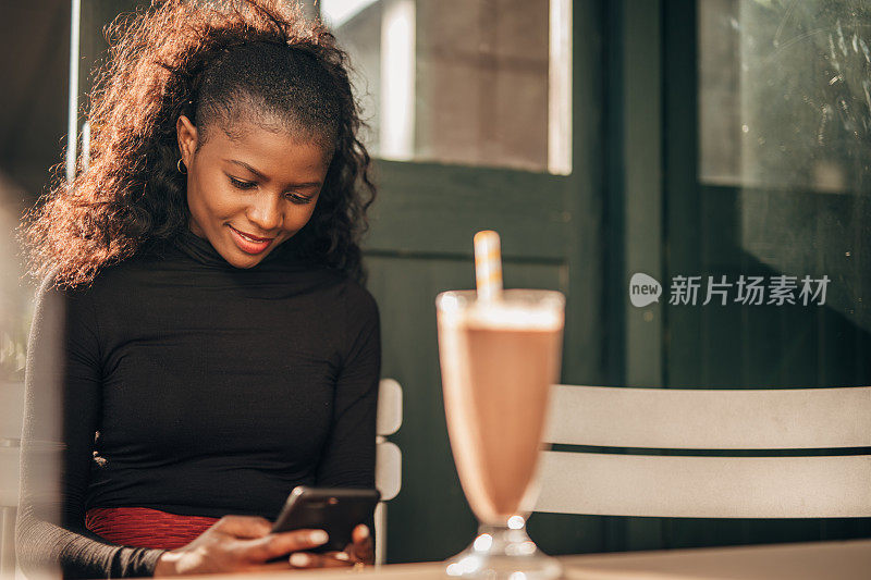 一名黑人女性独自坐在路边的咖啡馆里用着智能手机