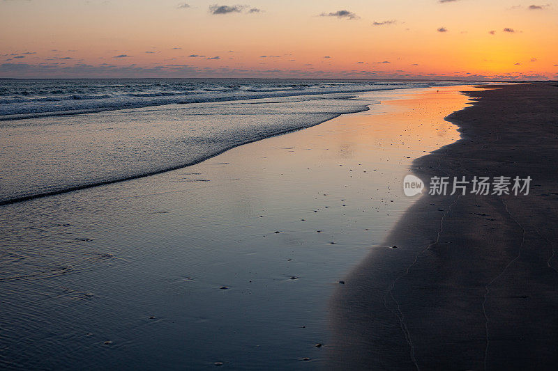 在日落后的海滩上，橙色的辉光在沙滩上反射出浅浅的海浪