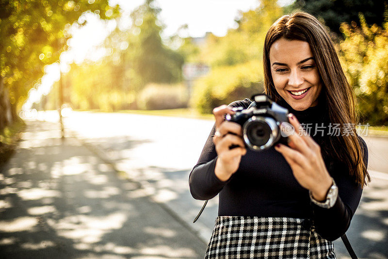 一个年轻的女人走在街上，用她的数码相机拍摄周围的环境