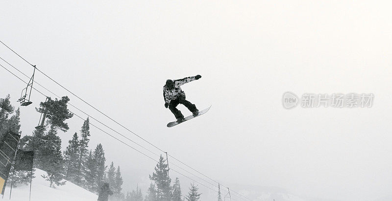 一个滑雪板在完整的冬季装备试图在一个森林和滑雪跳跃背景在埃尔多拉滑雪度假村附近博尔德，科罗拉多州在一个下雪的，阴天的伎俩