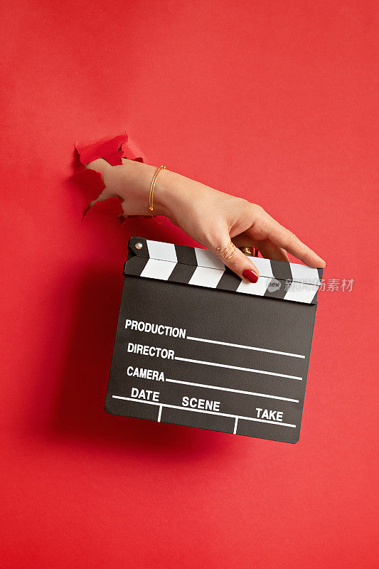 女人手握电影拍板通过孔在红色的纸背景。在工作室里制作视频电影。电影制作拍板，视频博客，电影创意