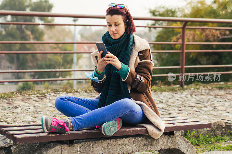 年轻女子使用电话在城市公园股票照片
