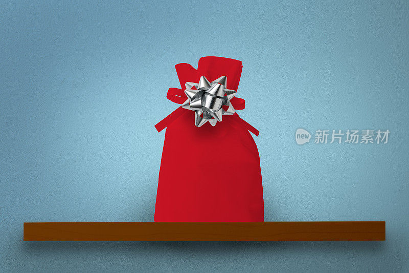 蓝色墙壁上的木架上挂着一个带丝带的红色礼品袋
