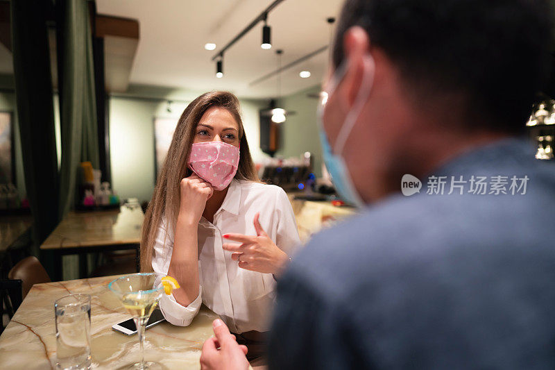 年轻女子戴着防护面罩在晚上在酒吧约会，聊天和享受