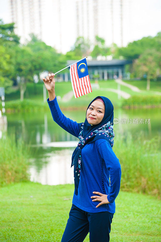 年轻的马来西亚妇女挥舞着马来西亚国旗，带着高昂的爱国主义精神在社区花园庆祝独立日