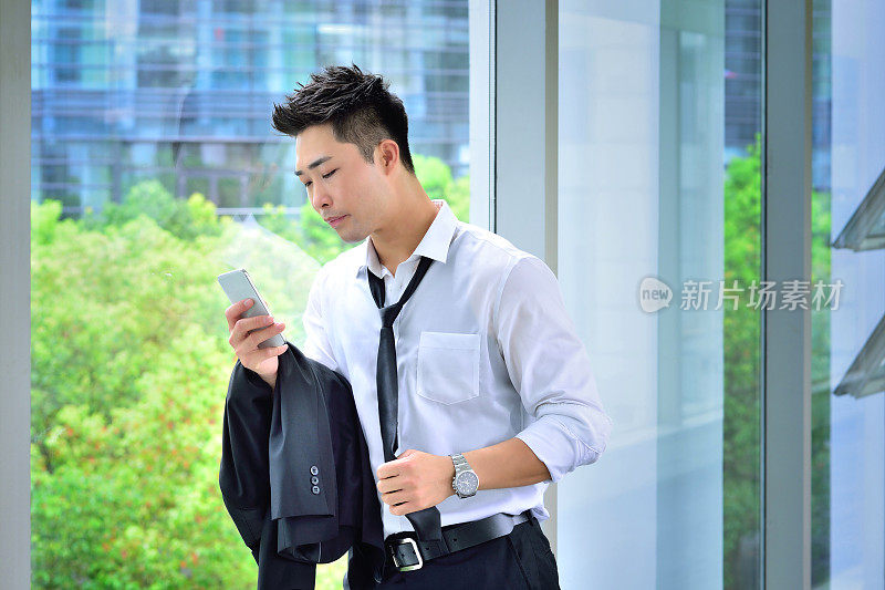一名亚洲男子倚靠在玻璃窗上看电话