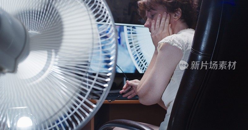 一个女人正试图在家里的台式电脑前工作，忍受着炎热的天气和使用电风扇
