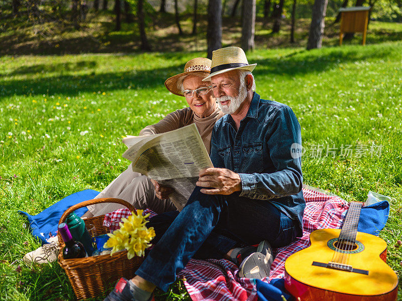 一对老年夫妇在看报纸，享受野餐