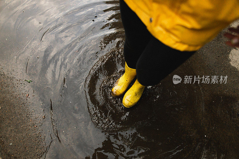 黄昏时分，一个穿着防水衣服的女人站在街上肮脏的水坑上