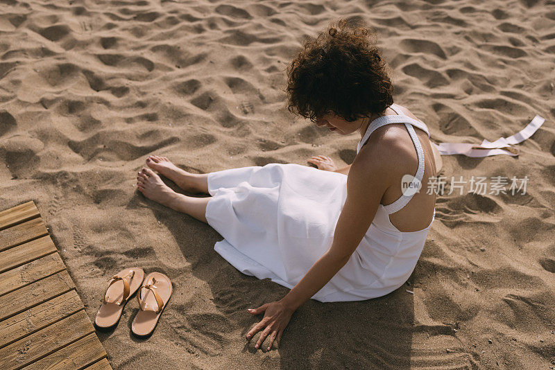 一个陌生的年轻女子穿着白色的裙子，坐在沙滩上的沙子上