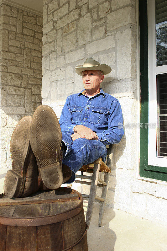 牛仔在门廊钉桶桌上的旧椅子上休息