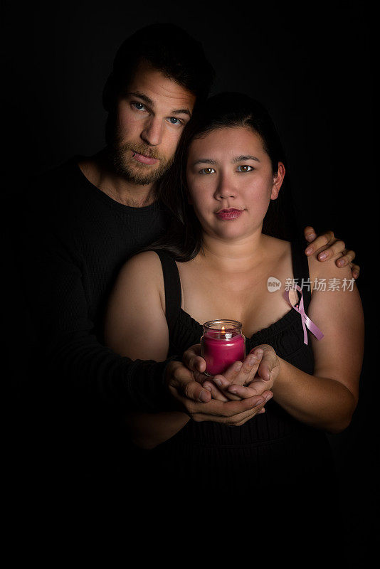 一对夫妇手拿蜡烛，佩戴乳腺癌关怀丝带