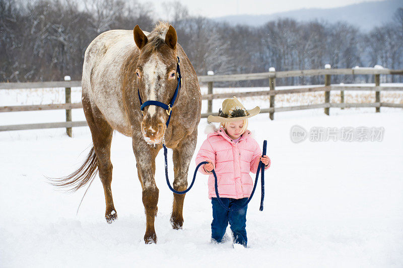 小女孩牵着大马穿过白雪覆盖的农田