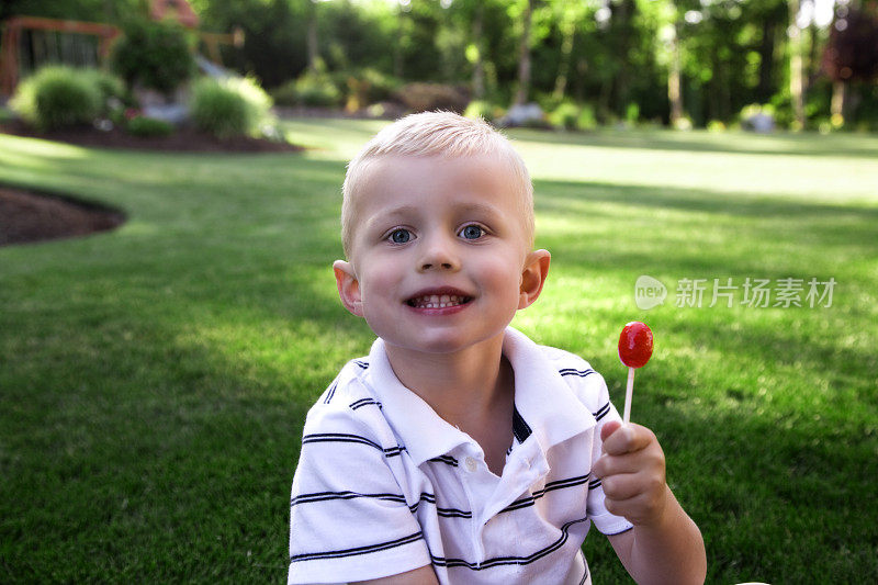 蹒跚学步的男孩在家里的庭院绿化草地棒棒糖