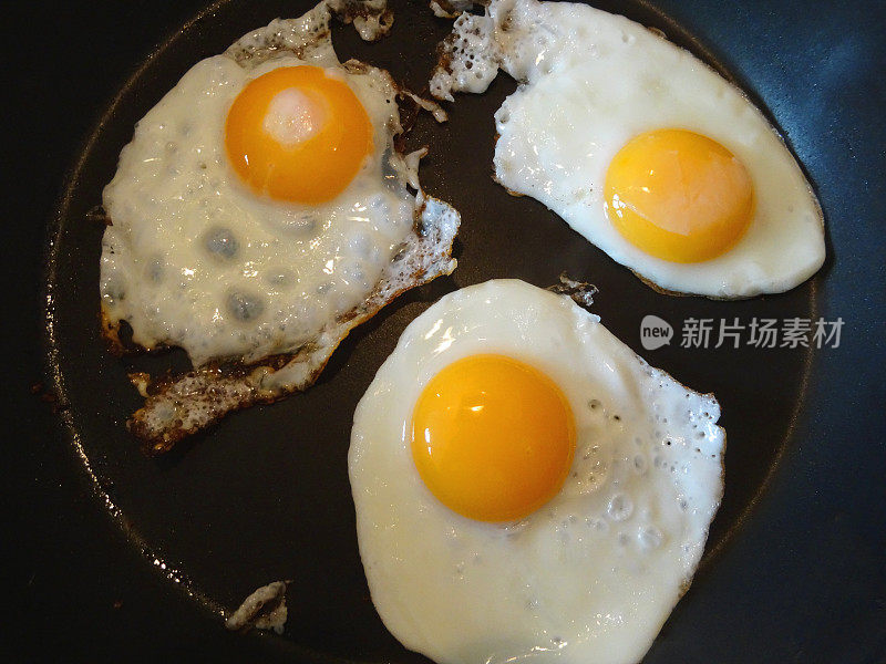 三颗煎蛋在煎锅里煎，全英式早餐