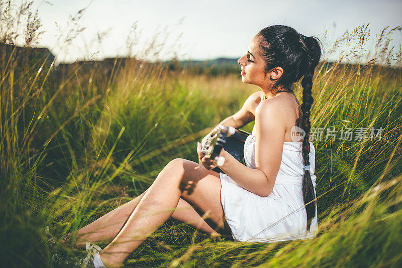 在草地上弹吉他的漂亮年轻女子