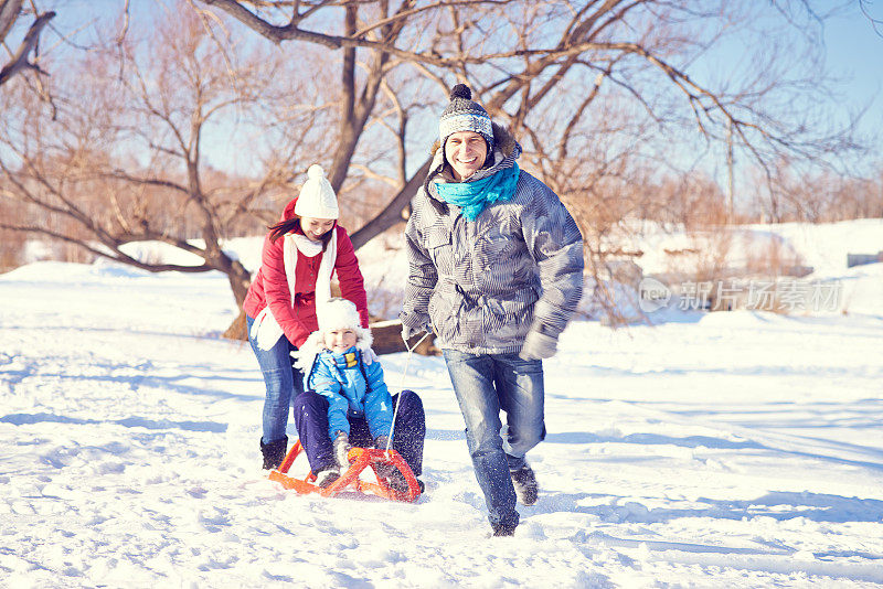 快乐的男人拉着他的妻子和儿子在雪橇上