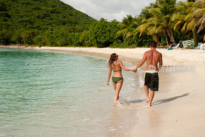一对蜜月夫妇手牵着手沿着热带海滩散步