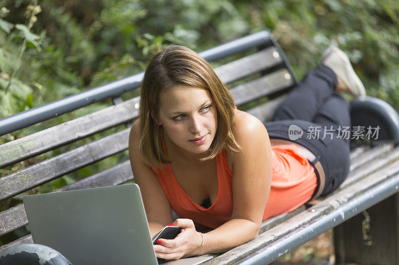 坐在长椅上摆弄电脑的年轻女子